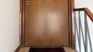 Puerta de madera con manija de latón, placa con un número, un escalón de mármol y una barandilla de metal.