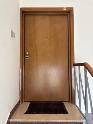 A wooden door with a brass handle and a number plate, a marble step, and a metal railing. - Penthouse San Francesco (Siena)