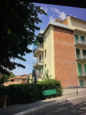 Un edificio de varios pisos con balcones, un banco verde y un cielo despejado.
