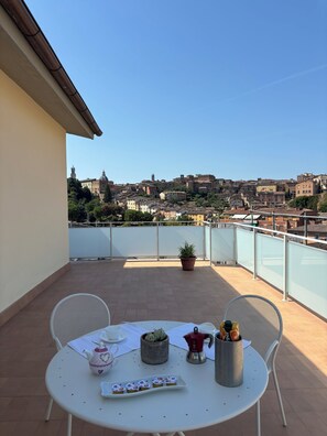 Une table ronde entourée de chaises, sur un balcon donnant sur une vue panoramique de la ville.