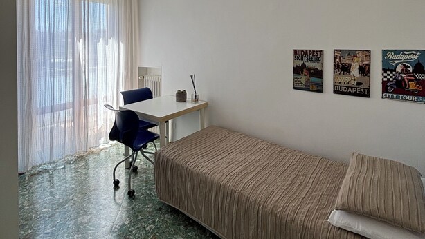 Una habitación con cama, escritorio, silla, lámpara colgante y tres carteles en la pared.