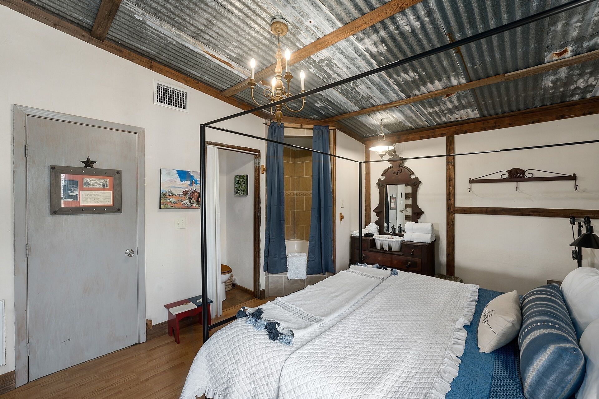 Une chambre à coucher avec un grand lit, une commode en bois, un miroir et un lustre.