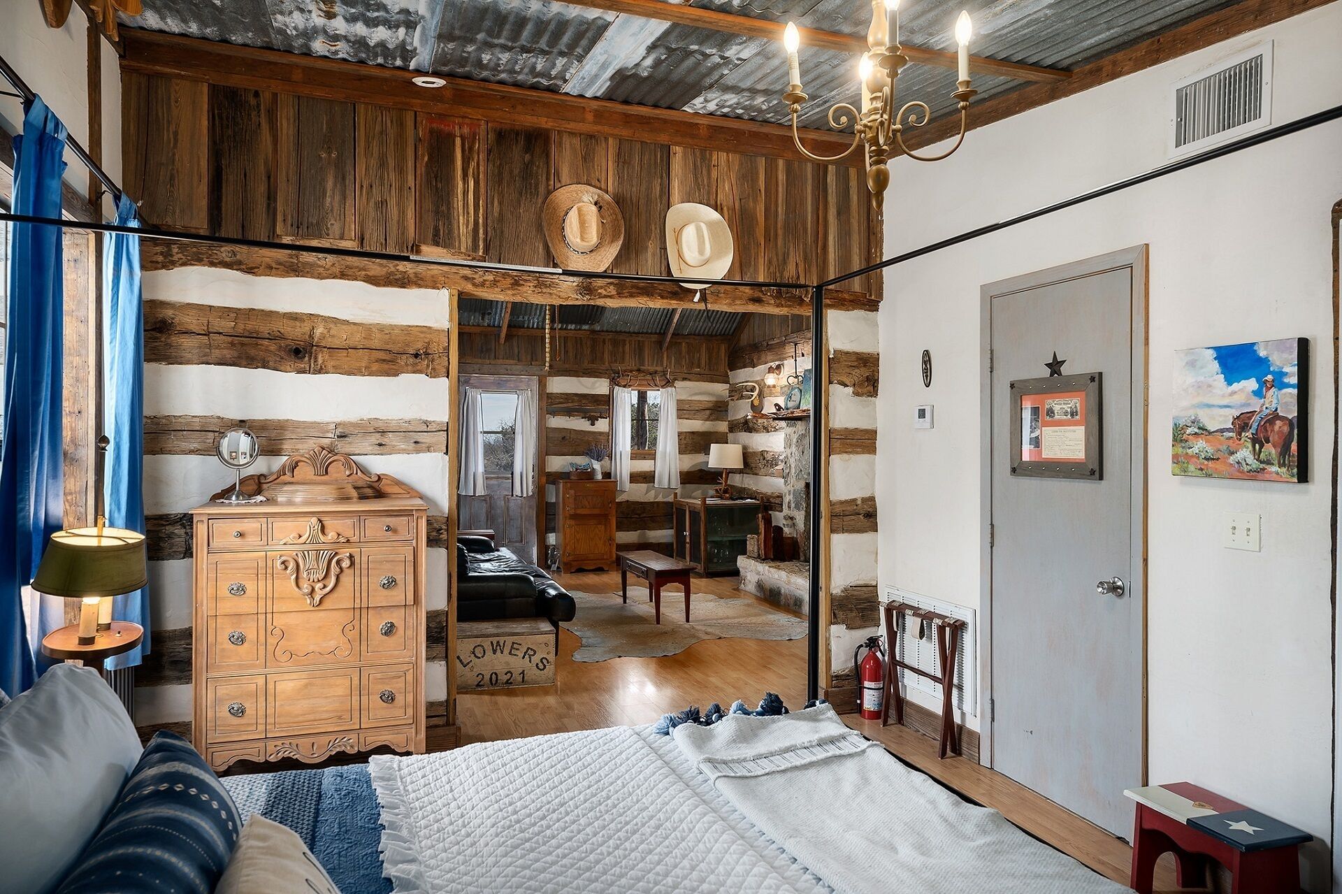 L’intérieur d’un chalet rustique, avec une commode en bois, un lit recouvert d’une courtepointe blanche, un lustre et une porte ornée d’une étoile.