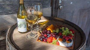 Une bouteille de vin, deux verres et une assiette de fruits sur un tonneau en bois.