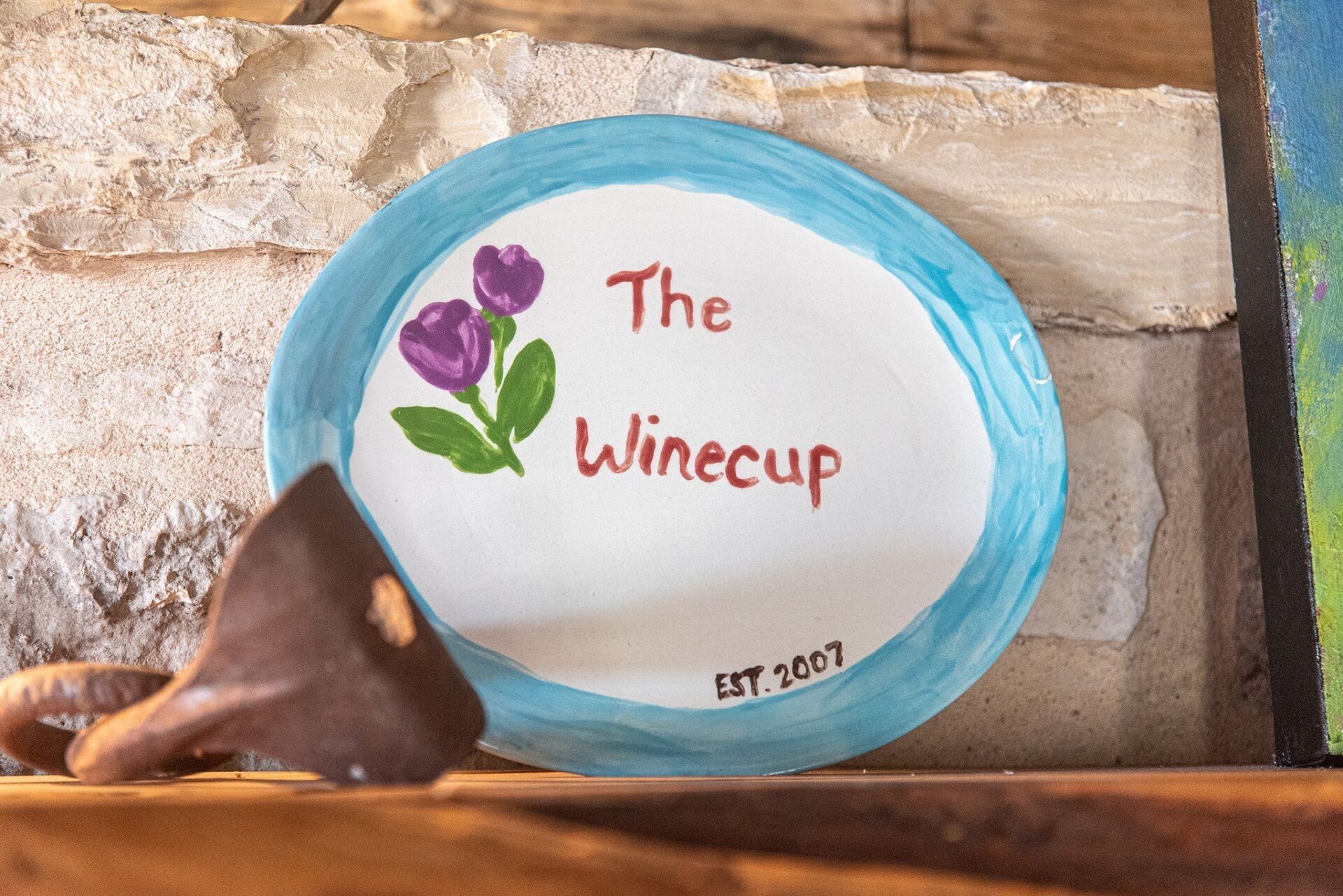 A sign with the text "The Winecup" and "EST. 2007" against a stone wall background.