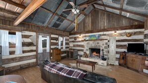 L’intérieur d’un chalet rustique, avec une cheminée en pierre, un canapé en cuir, des meubles en bois et un téléviseur.