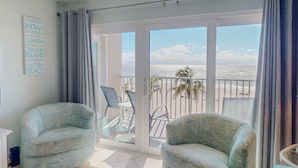 Ein Balkon mit zwei Sesseln, einem Tisch und Blick auf den Strand.