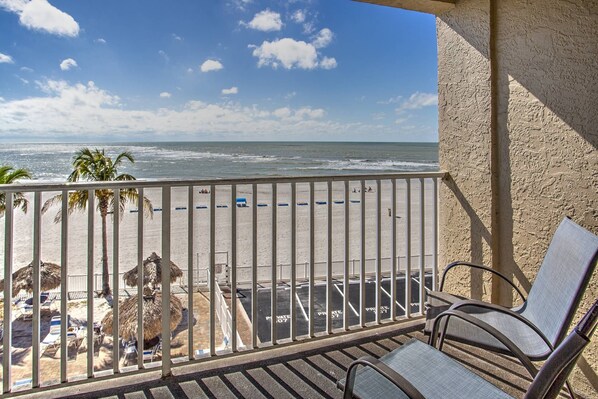 Un balcon avec vue sur la plage, comprenant des chaises longues et un parasol en chaume.