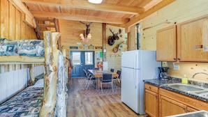Interior de una cabaña con comedor, cocina y una cama con un cabecero original.