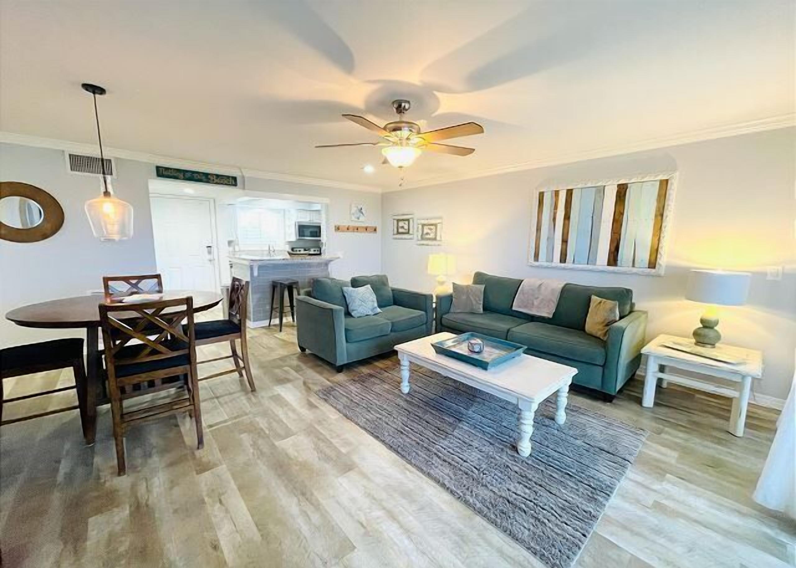 A modern living room with a dining area, a kitchen in the background, and a ceiling fan.