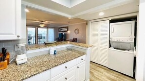 A kitchen with white cabinets, a granite countertop, a built-in oven, and a view of the outside. - Pool&Golf Views 2BR Retreat with FreeBeachService (Destin)