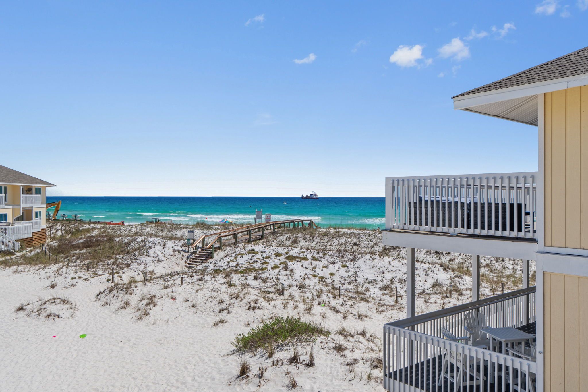 Blick auf einen Strand mit einer hölzernen Treppe, die zu einem weißen Gebäude mit Balkonen führt.