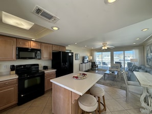 Enjoy cooking in the central island kitchen with a stove, microwave, and refrigerator, opening up to a spacious living area with a balcony view.