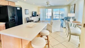 Una cocina moderna con una isla grande, un comedor con sillas blancas y un balcón con vistas.