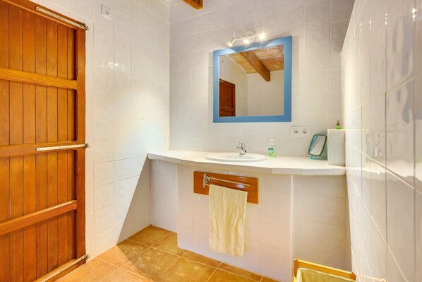 A bathroom with a wooden door, white tiled walls, a sink with a mirror above it, and a towel hanging on a rack. - VILLA CALVIA SA PLANA by PriorityVillas (Calvià)