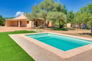 A swimming pool with a stone border, a grassy lawn, and a stone building with a tiled roof. - VILLA CALVIA SA PLANA by PriorityVillas (Calvià)