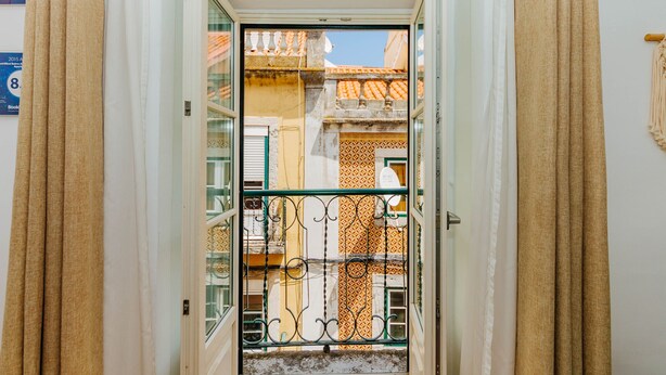 A doorway with a wrought iron gate, leading to a balcony with a tiled wall and a clear blue sky in the background. - RENT4REST BAIRRO ALTO CHARMING 1 BEDROOM APARTMENT (Lisboa ciudad)