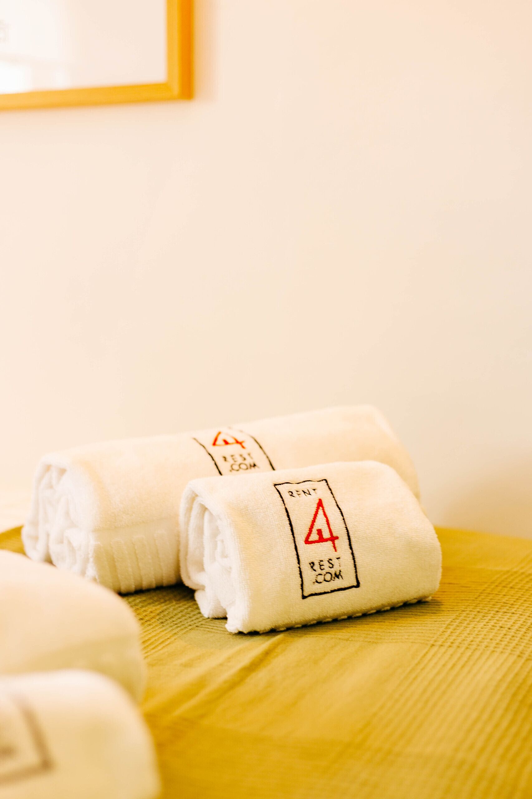 A neatly folded white towel with a red and black logo on a yellow bedspread.