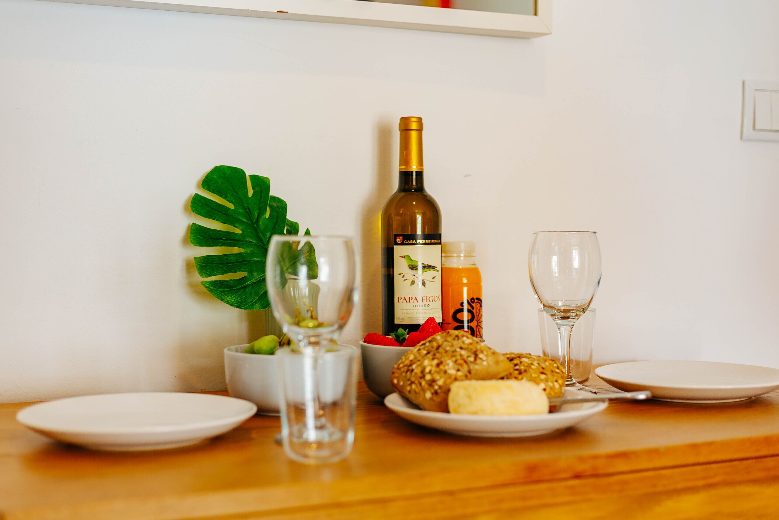 Una mesa con una botella de vino, una copa, un bol de fresas, una planta y un plato con un pastel.