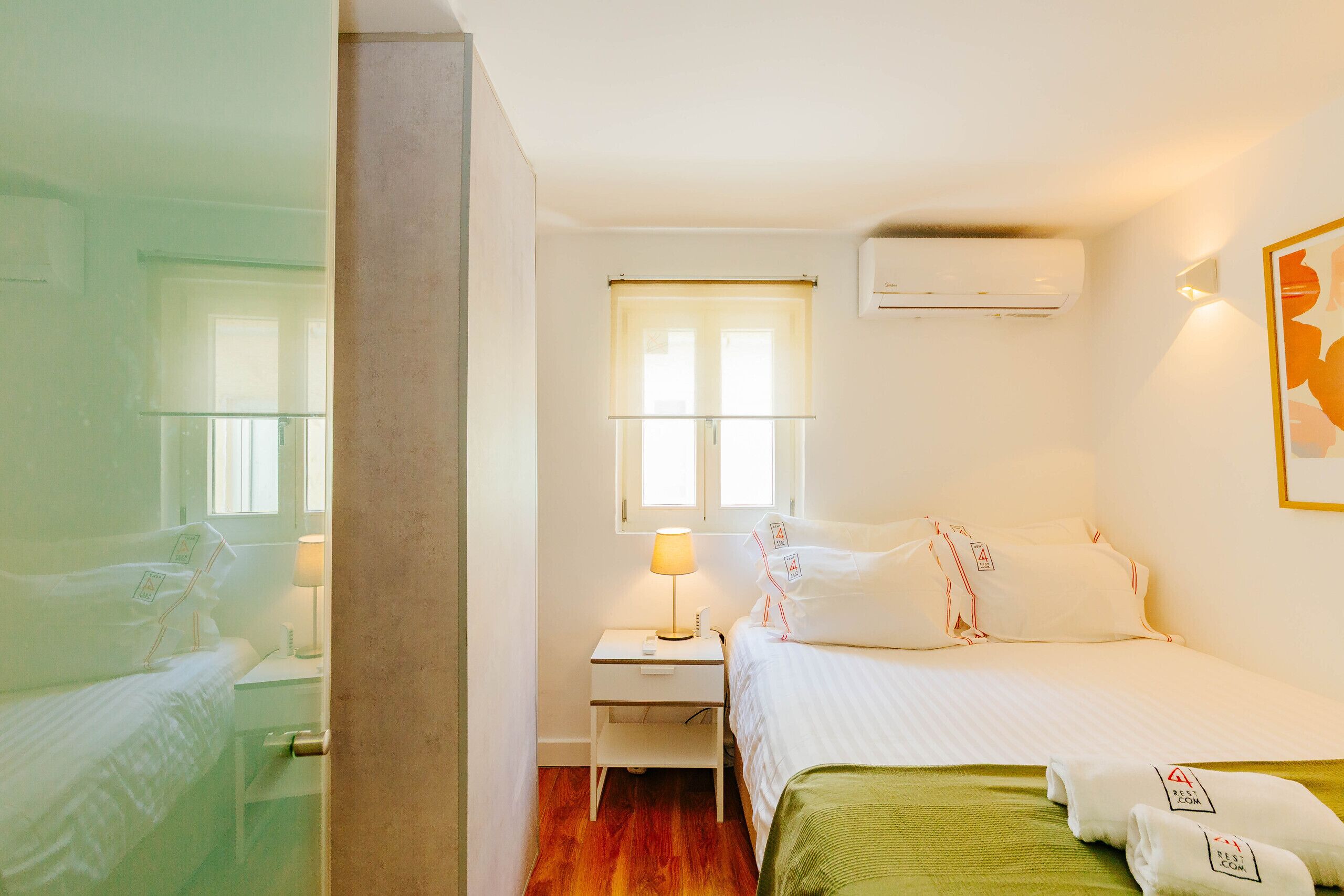 Een hotelkamer met een bed, nachtkastje met een lamp, een raam en een airconditioning.