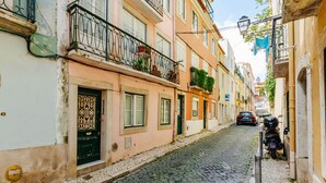 A narrow cobblestone street lined with pastel-colored buildings, a parked motorcycle, and a car in the distance. - RENT4REST BAIRRO ALTO CHARMING 1 BEDROOM APARTMENT (Lisboa ciudad)