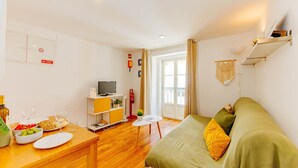 A well-lit room with a bed, a dining table with breakfast items, a TV, and a small table with a plant. - RENT4REST BAIRRO ALTO CHARMING 1 BEDROOM APARTMENT (Lisboa ciudad)
