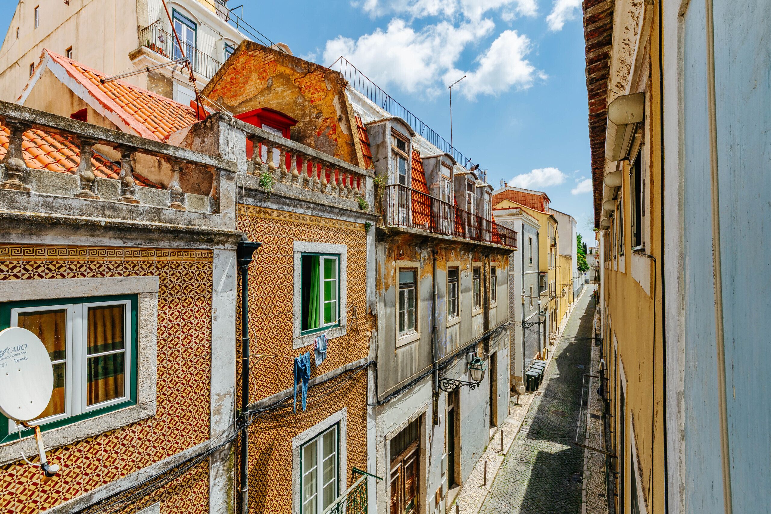 A narrow street with buildings featuring traditional architecture, including balconies and tiled roofs.