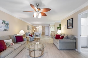 Ein geräumiges Wohnzimmer mit Deckenventilator, einem Glastisch und zwei Sofas.