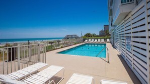 Piscina no terraço com vista para o oceano, cadeiras de descanso brancas e placa de salva-vidas.