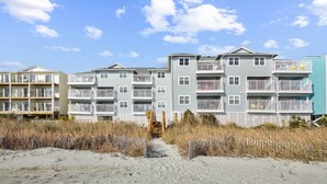 Um edifício residencial com várias andares e varandas, à beira da praia, com uma faixa de areia em primeiro plano.