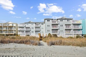 A beachfront multi-story residential building with balconies and a sandy beach in the foreground.