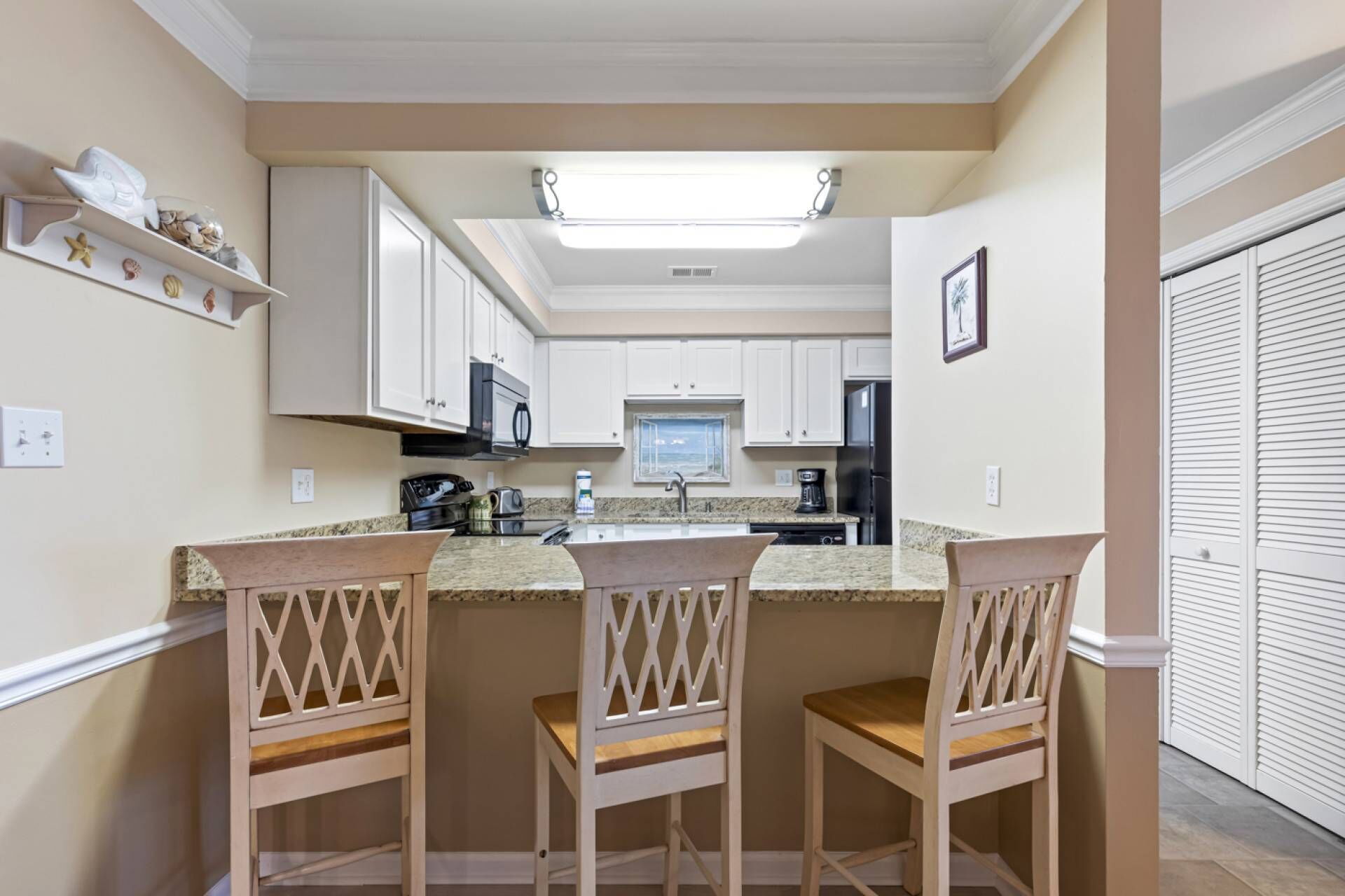 A kitchen with white cabinets, a central island with bar stools, a microwave, and a refrigerator.