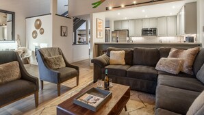 A modern living room with a large sectional sofa, a coffee table with a magazine, and a dining area with a kitchen in the background.