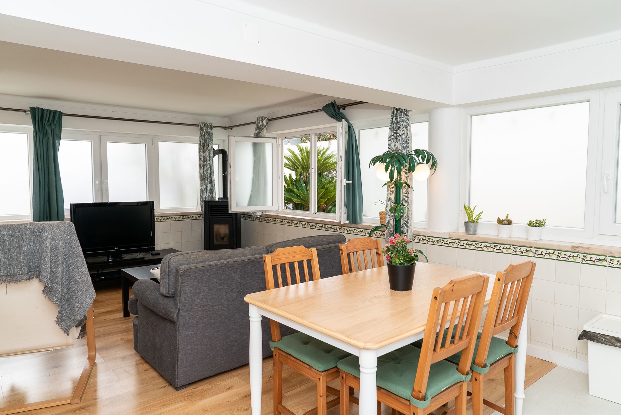 A cozy living area with a sofa, a TV, a dining table with chairs, and a kitchen area with a window.