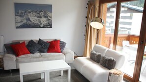 En stue med en sofa, et hvidt sofabord og et maleri af et bjerglandskab.