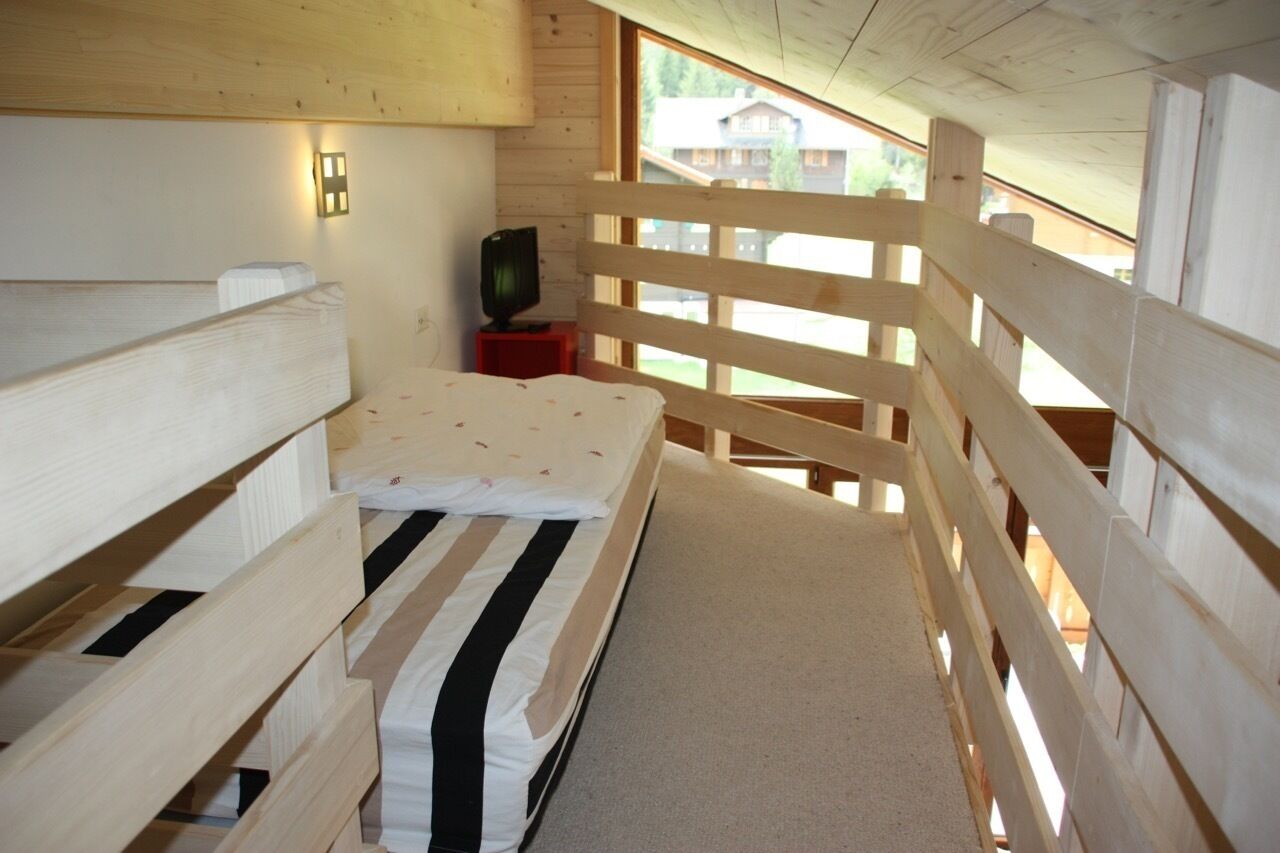 Habitación de cabaña de madera con literas, un televisor pequeño sobre un soporte rojo y una ventana con vistas a un área boscosa.