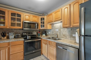 A kitchen with wooden cabinets, a stainless steel refrigerator, a microwave, an oven, and a sink.