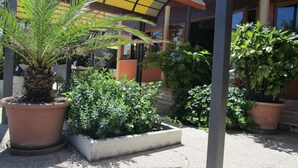 A courtyard with potted plants, a concrete planter, and a building with a yellow awning. - Albergo Hotel Primavera (Senigallia)