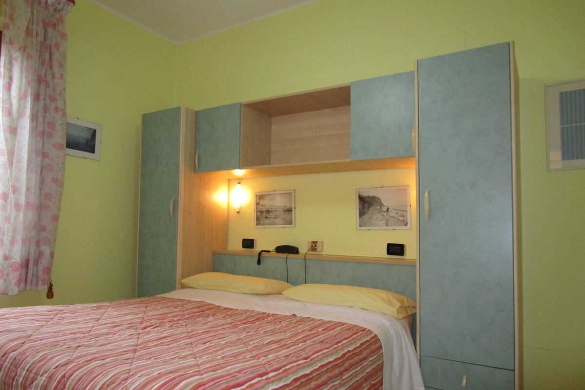 Quarto com cama, mesa de cabeceira, espelho e luminária na parede.