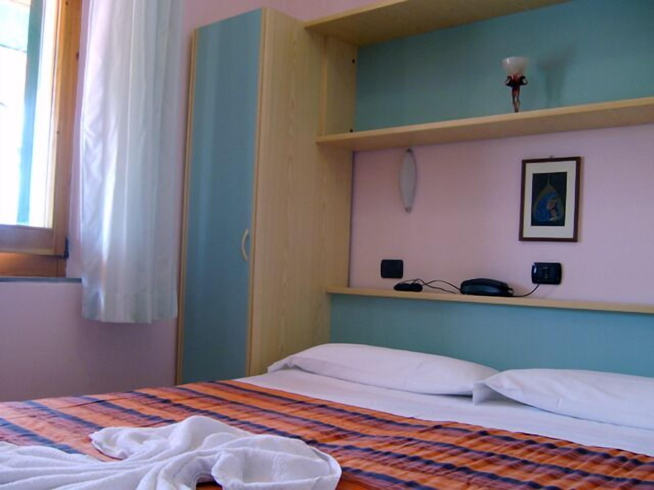 Une chambre à coucher avec un lit, une table de chevet, une lampe fixée au mur et un tableau encadré.
