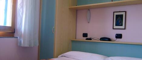 Une chambre à coucher avec un lit, une table de chevet, une lampe fixée au mur et un tableau encadré.