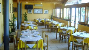 A restaurant with multiple tables set for dining, wooden beams on the ceiling, and large windows on one side. - Albergo Hotel Primavera (Senigallia)