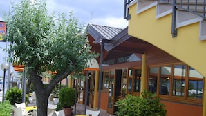 An outdoor seating area with white chairs and yellow tablecloths, surrounded by potted plants and a building with a yellow facade. - Albergo Hotel Primavera (Senigallia)