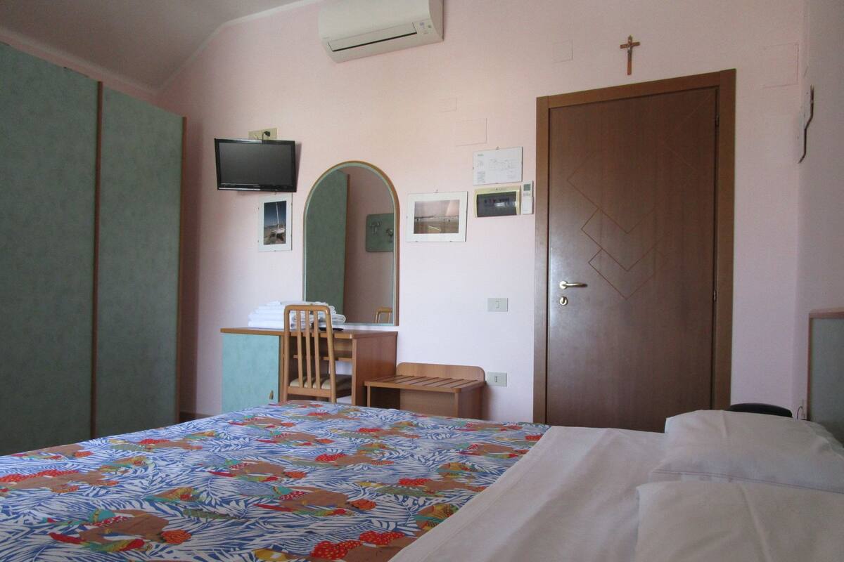 Quarto com cama, cadeira, escrivaninha, televisão e porta.