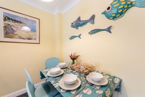 Un coin repas avec une table dressée pour quatre personnes, décorée d’une nappe à motifs de poissons.
