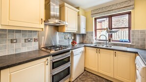 A kitchen with a gas stove, oven, and dishwasher, with beige cabinets and a window with a view.