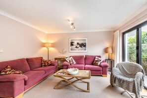 Un salon avec deux canapés rouges, une table basse en bois et un fauteuil. Un tableau encadré est accroché au mur et une lampe se trouve sur une table d’appoint.