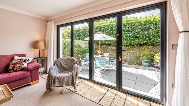 A living room with a red sofa, a covered chair, and a table with chairs outside a sliding glass door.