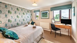 A bedroom with a bed, a desk, a chair, a radiator, and a window with a view.