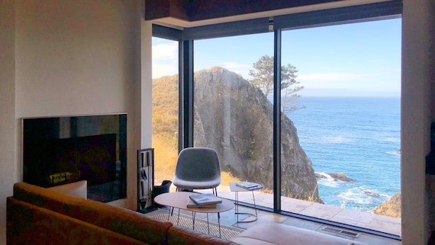 A modern living room with a large window overlooking a coastal cliff and ocean.